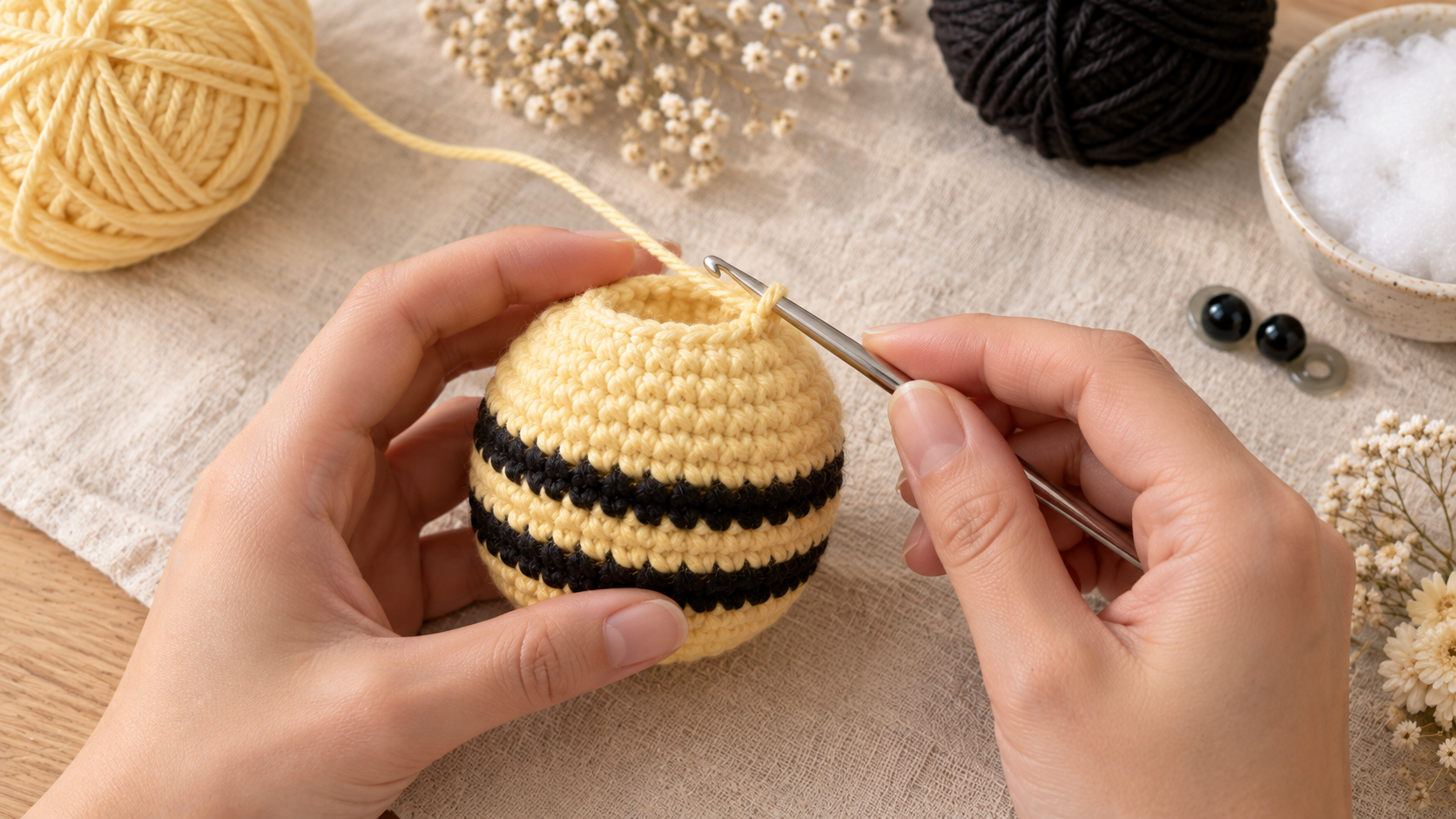 Close-up of two hands holding a small yellow crocheted ball and working the next round with a silver 3.5 mm steel crochet hook, pale yellow yarn feeding in from the left