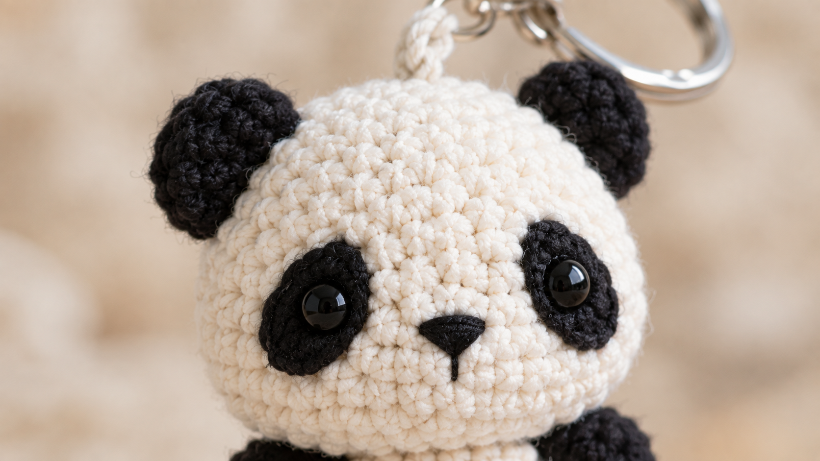 Extreme close-up macro of the finished crochet panda keychain head showing white cotton stitches, glossy black safety eyes surrounded by embroidered almond patches, small satin-stitched nose and mouth, and two round black ears sewn to the top